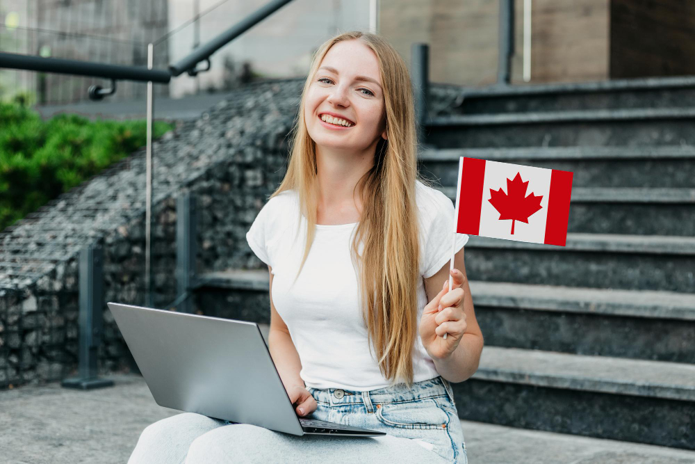 Canada’s Future Depends on Immigration—Here’s Why 2 female student sitting stairs with laptop holding small canada flag